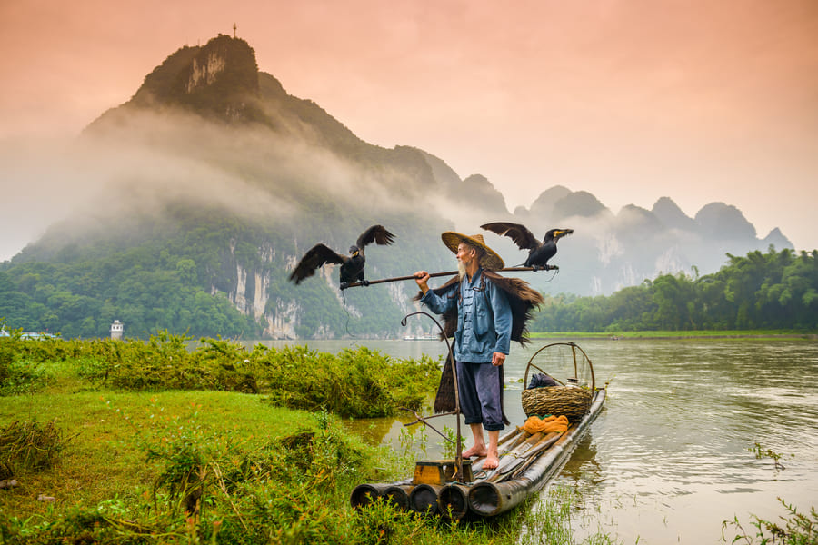 hombre pescador en una balsa en el rio Yulong con comida de fondo un paisaje de montañas y aves